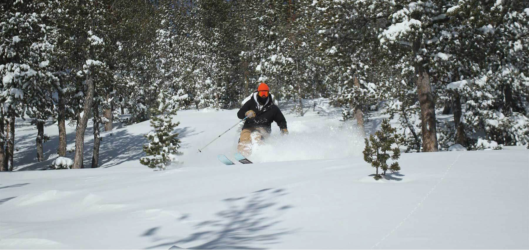 man in orange hat skiing light powder in the trees